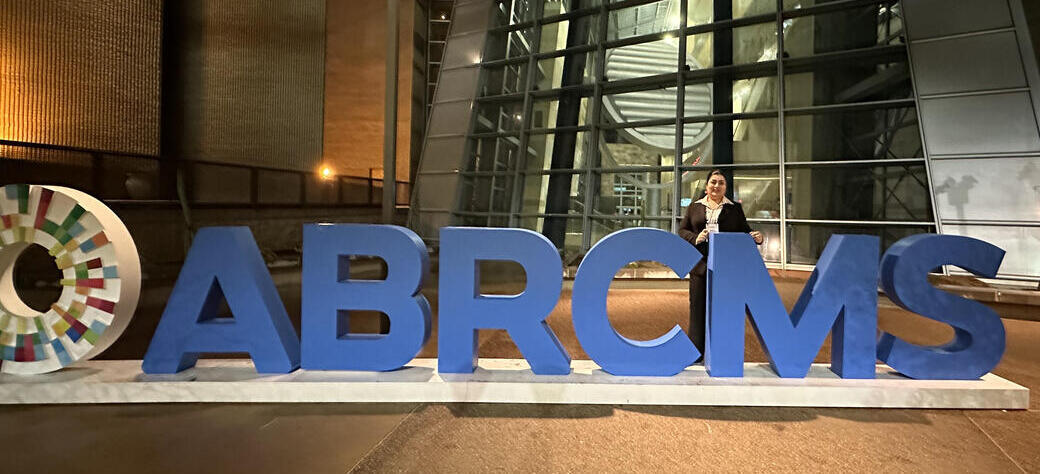BSP student Ameneh Gharabi stands outside with large blue letter sculptures that spell "ABRCMS"