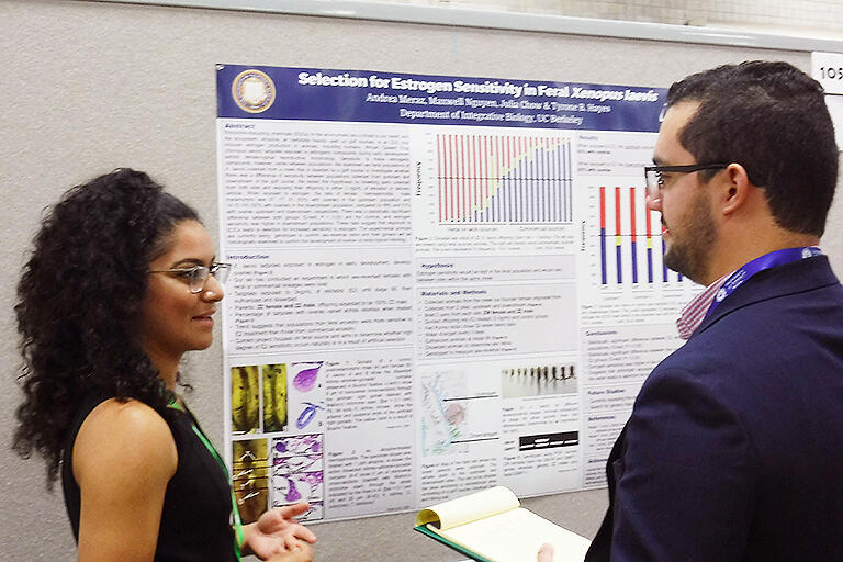 Meraz standing in front of her research poster talking to a man with a clipboard.