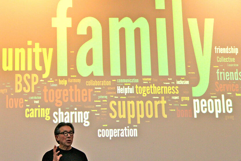 John Matsui giving a talk with a word cloud on the screen behind him
