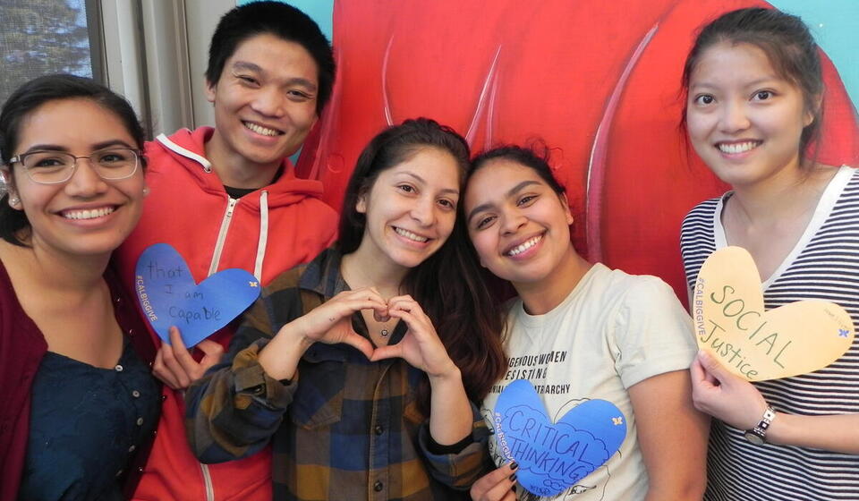 five students smiling at the camera with heart signs