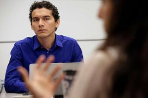 BSP alum Juan Vasquez sitting at a discussion table listening to a women talking in the foreground.
