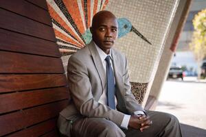 BSP alum Dr. Anthony Muiru seated on a wooden bench on the UCSF campus.