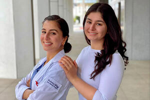 Nazieen on left wearing the JMP white coat and scrubs, Nilufar on right.
